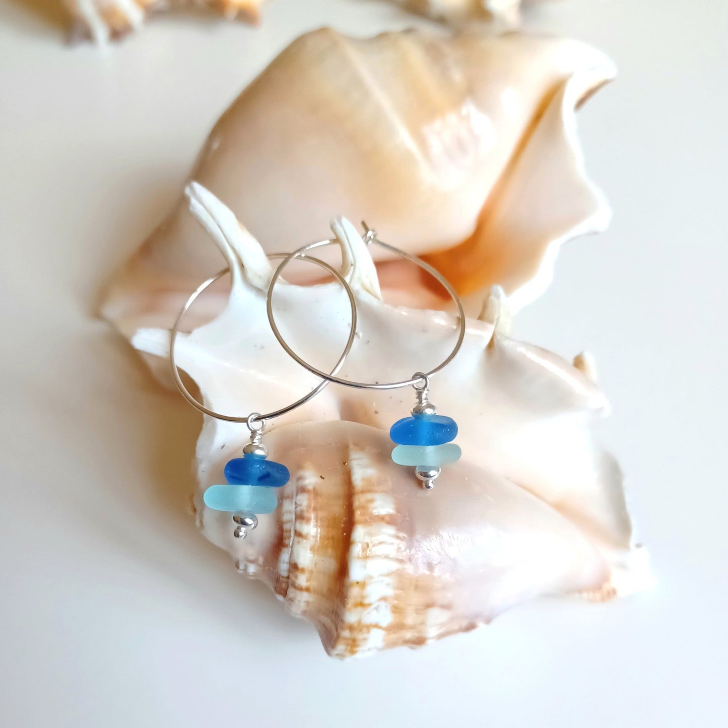 Silver hoop earrings with blue and light blue sea glass mini stacks hanging from the hoop.