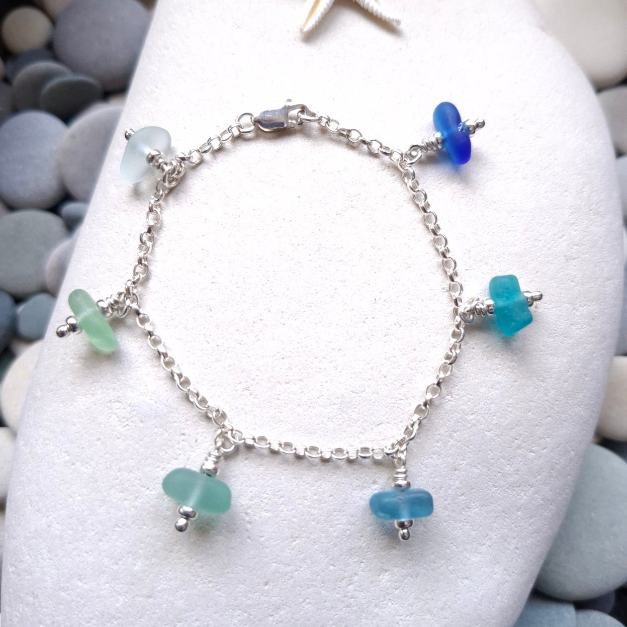 A silver chain bracelet with five small sea glass jewels in various coastal colours.