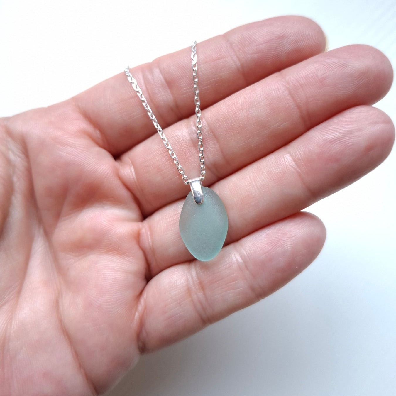 A silver chain necklace with an aqua sea glass pendant.