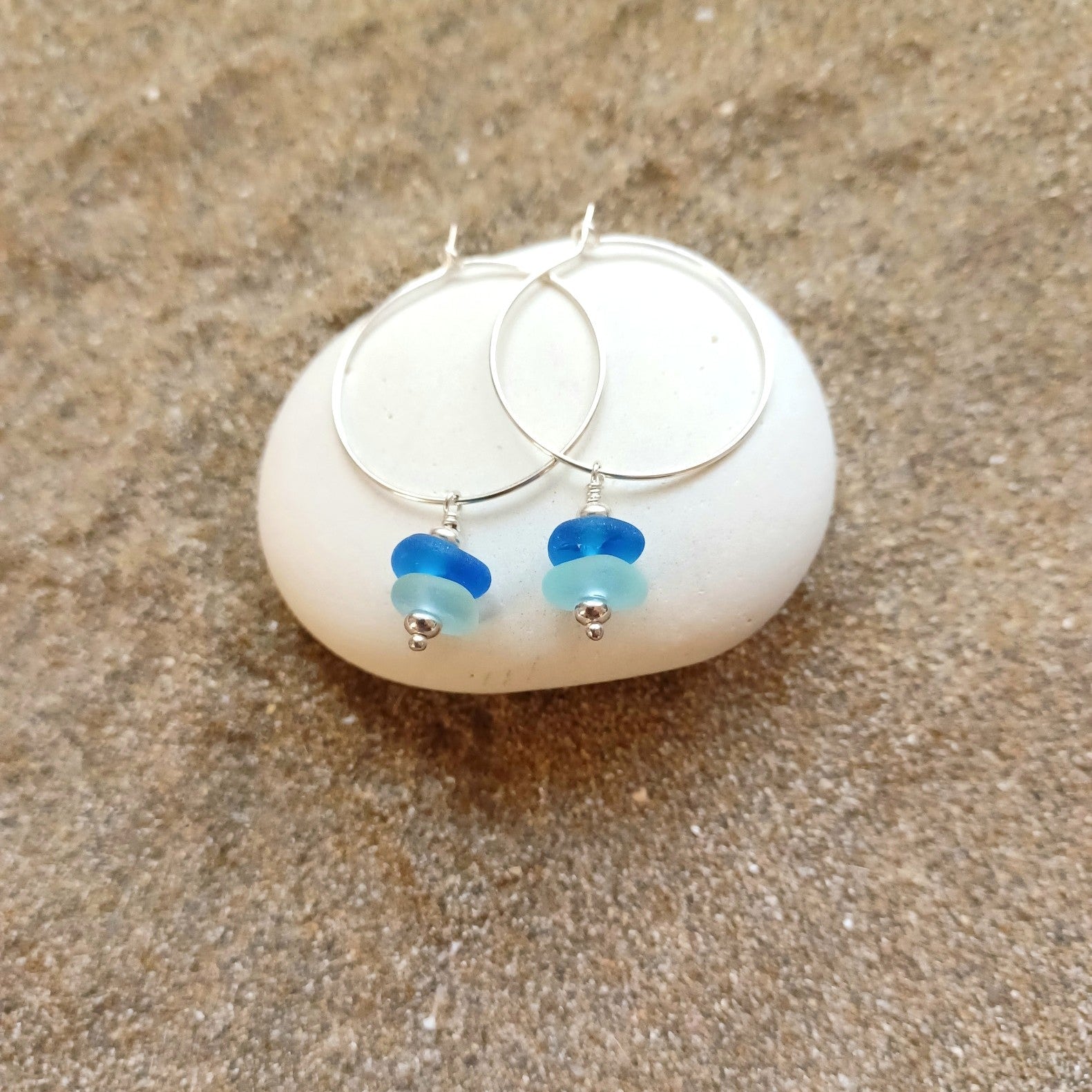 Silver hoop earrings with blue and light blue sea glass mini stacks hanging from the hoop.