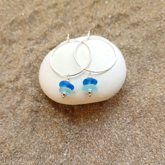 Silver hoop earrings with blue and light blue sea glass mini stacks hanging from the hoop.