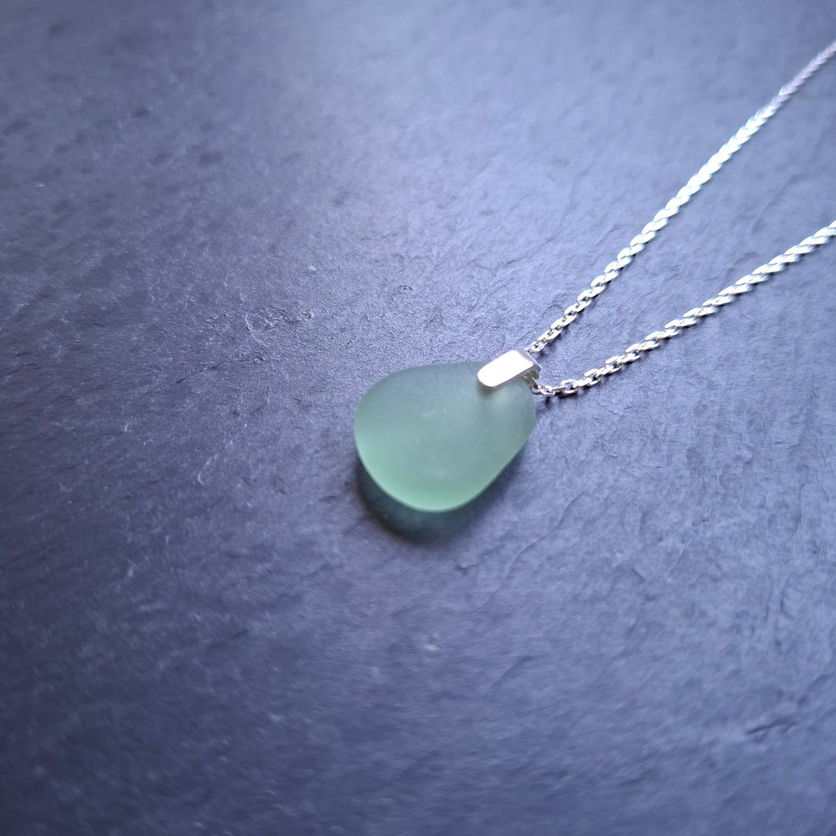 A delicate silver chain necklace featuring a light green sea glass pendant.