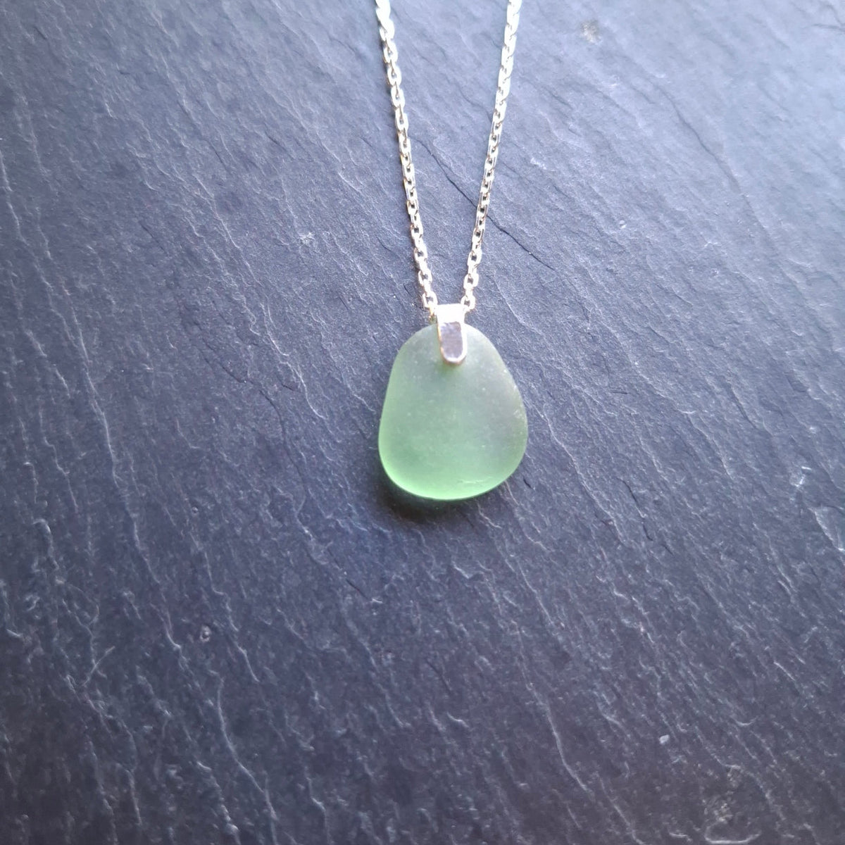 A delicate silver chain necklace featuring a light green sea glass pendant.