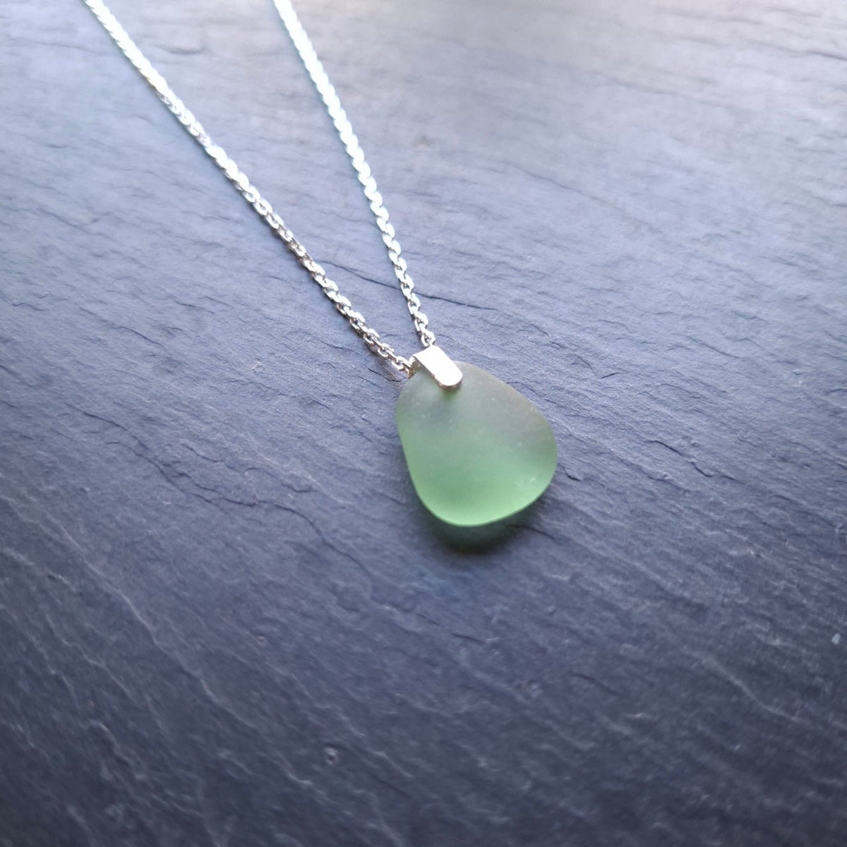 A delicate silver chain necklace featuring a light green sea glass pendant.