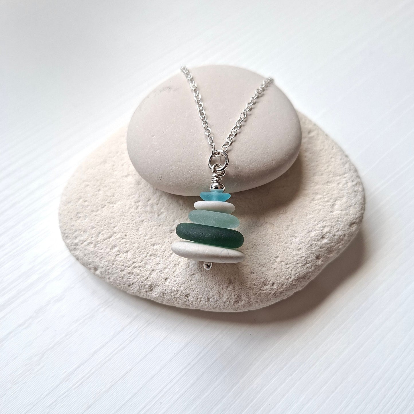 A sea glass pendant necklace with beach pebbles and a silver bead on top.