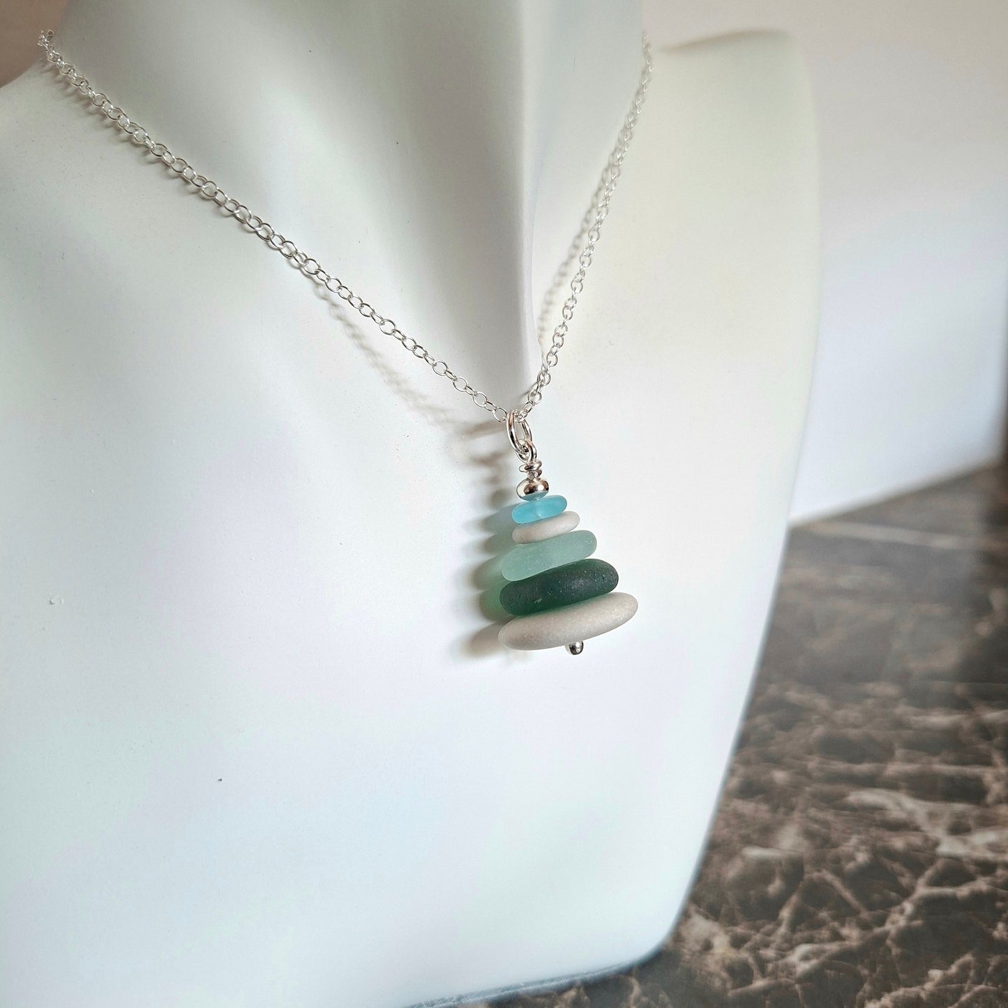 A sea glass pendant necklace with beach pebbles and a silver bead on top.