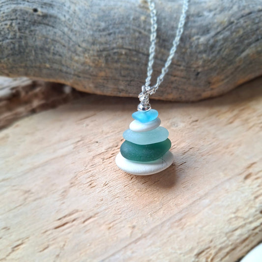 A sea glass pendant necklace with beach pebbles and a silver bead on top.