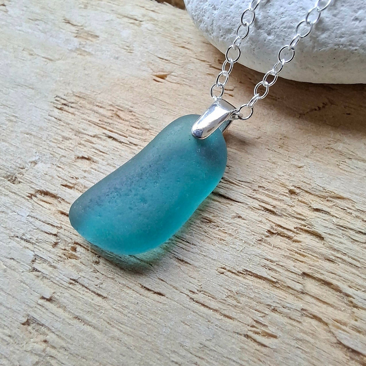 A teal sea glass pendant necklace on a sterling silver chain.