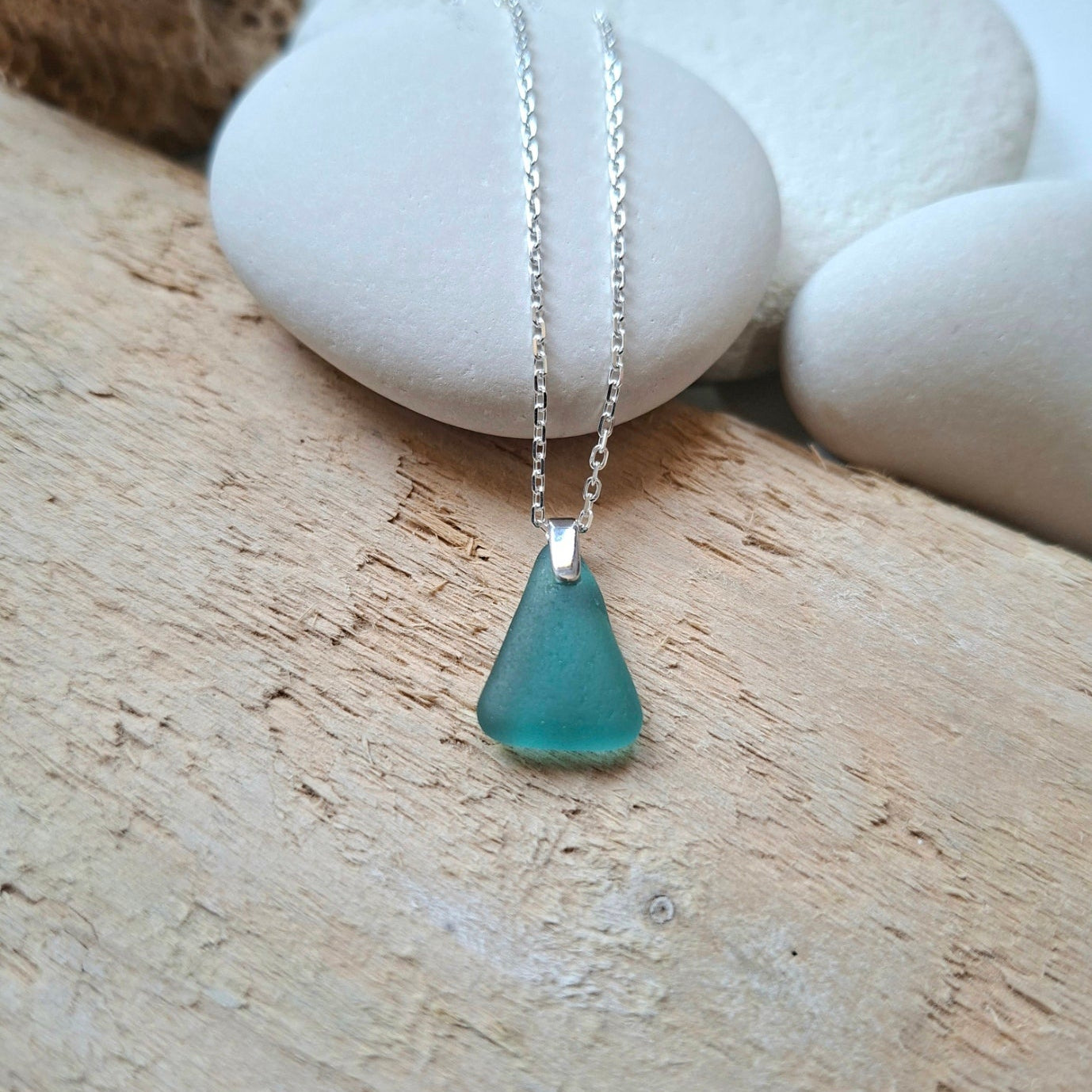 A silver chain necklace with a small triangular sea glass pendant in teal green.