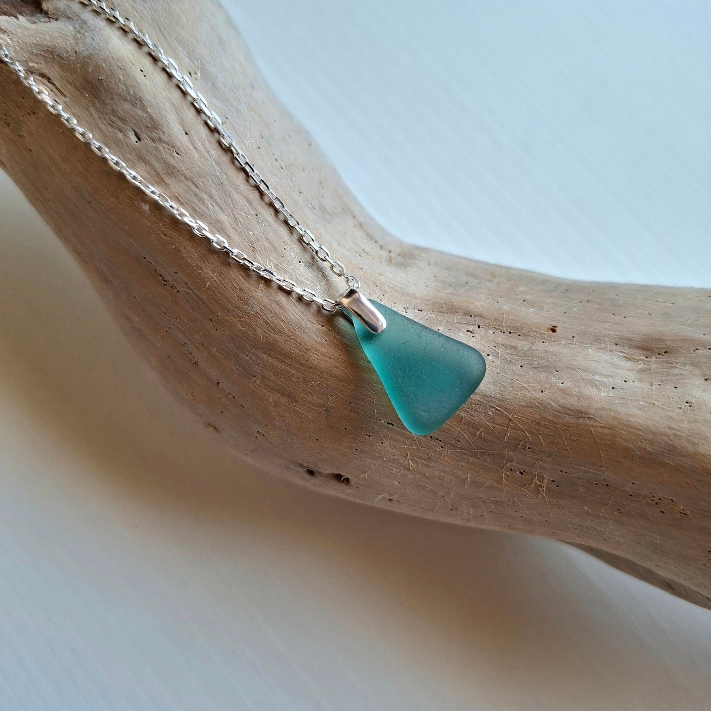 A sea glass pendant necklace in a teal color on a silver chain.