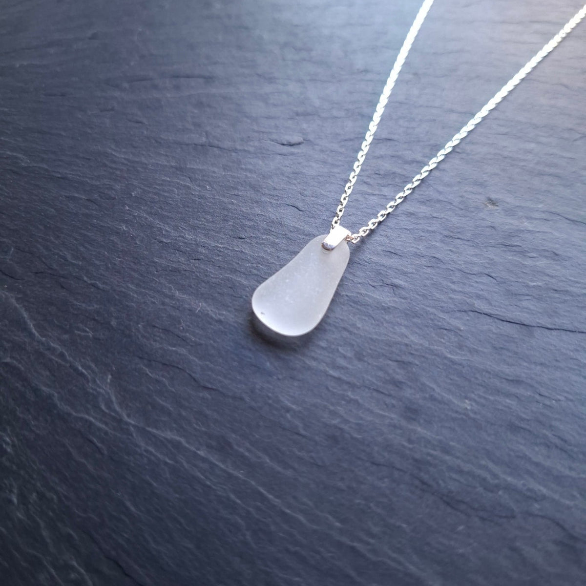A delicate silver chain necklace featuring a white sea glass pendant.