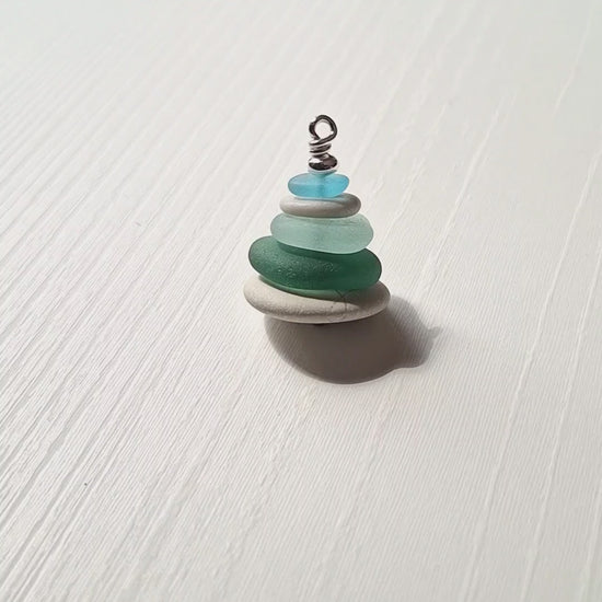 A sea glass pendant necklace with beach pebbles and a silver bead on top.