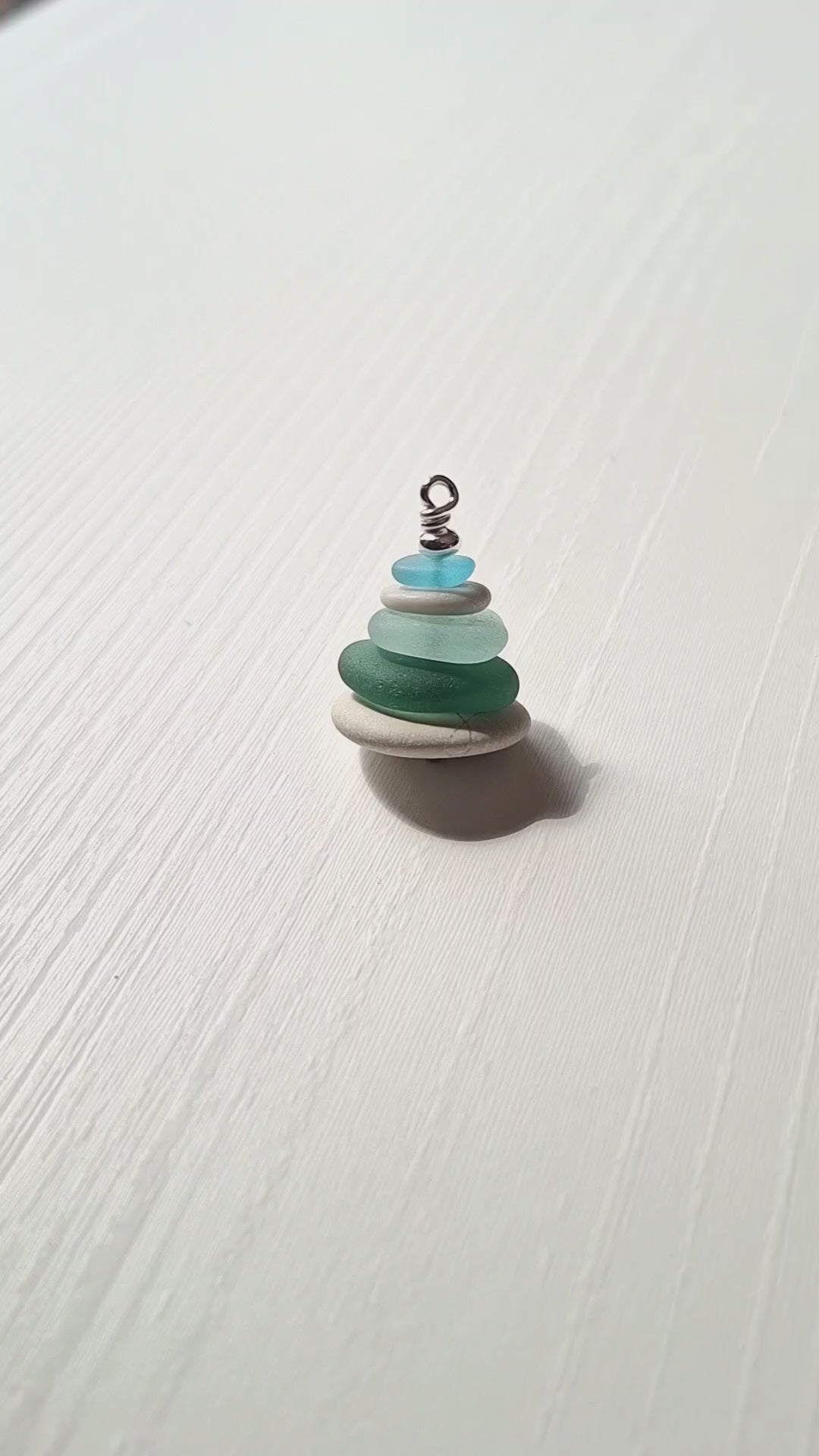 A sea glass pendant necklace with beach pebbles and a silver bead on top.